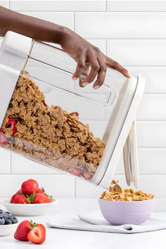 a person pouring cereal into a bowl with strawberries and blueberries on the side