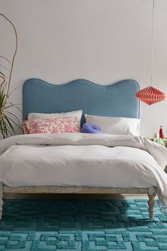 a bed with blue headboard and pillows in a white room next to potted plants