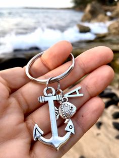 a person holding an anchor and fish keychain in their hand near the ocean