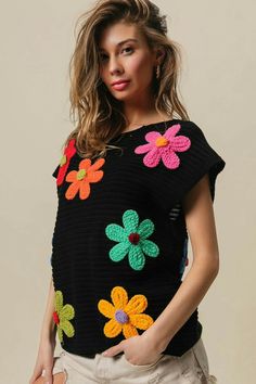 a woman wearing a black sweater with crochet flowers on it and her hands in her pockets