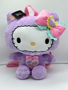 a purple hello kitty stuffed animal with a pink bow on its head, sitting in front of a white background