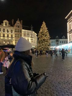 a woman standing in front of a christmas tree on a city street with lots of people