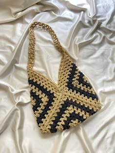 a crocheted purse laying on top of a white bed covered in sheets and blankets