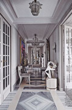 an elegant hallway with chandelier, chairs and paintings on the walls in front of glass doors