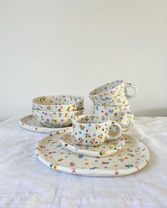 a table topped with plates and cups filled with confetti on top of a white cloth