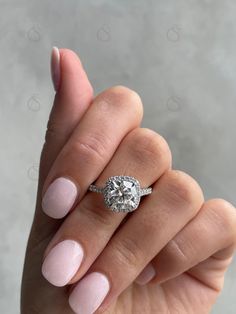 a woman's hand holding a ring with a diamond on it and pink nail polish