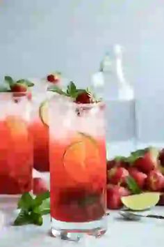 three glasses filled with drinks and garnished with limes, strawberries, and lime wedges