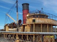 an old wooden boat sitting on top of a body of water next to a chain link fence