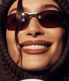 a woman wearing sunglasses and holding a coffee cup in front of her face, smiling