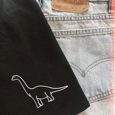 a t - shirt with a dinosaur drawn on it is next to some denim jeans