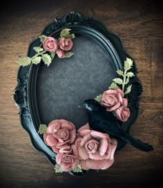 a black bird sitting on top of a wooden table next to pink flowers and leaves