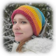 a woman wearing a multicolored knitted hat in front of snow covered trees