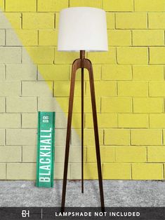 a floor lamp next to a yellow brick wall with a green sign on the side