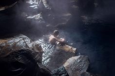 a man sitting on top of a large rock next to a body of water with steam coming out of it