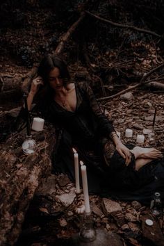 a woman sitting on the ground with candles in front of her, surrounded by rocks and branches