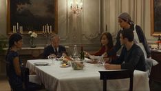 a group of people sitting around a table with food and wine glasses in front of them