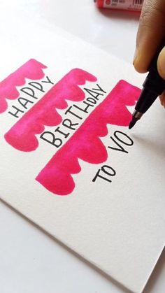 a person writing on a piece of paper that says happy birthday to you with pink ink