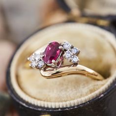 This lovely by-pass style ring is centered with one (1) oval mixed cut natural ruby set into a four-prong head. The ruby is bordered to each side by four (4), prong set, round single cut diamonds. The ring measures 9.5mm at the top, rises 5.5mm above the finger, tapering to 1.2mm wide and 1.2mm thick at the base of the shank. This ring is currently a size 5. Classic Ruby Cluster Ring With Gemstone, Classic Ruby Ring With Marquise Cut And Prong Setting, Oval Ruby Jewelry With Brilliant Cut For Weddings, Oval Ruby Ring With Rose Cut Diamonds For Promise, Heirloom Ruby Ring With Accent Stones, Classic Ruby Birthstone Ring With Rose Cut Diamonds, Oval Ruby Diamond Ring With Prong Setting, Ruby Cluster Ring With Accent Stones, Heirloom Ruby Ring With Prong Setting