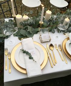 the table is set with white and gold plates, silverware, greenery and candles