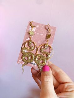 Celestial snake earrings. The earrings are big and will surely catch people's eyes but luckily they weigh next to nothing.  The snake is made out of resin and glitter. All the brass details and hooks are hypoallergenic and goldplated.  The whole earring measures 10 cm/3.9 inches. If you don't hooks you can choose rings or clipons in the menu. Both options are also goldplated and nickelfree. The rings are small closed hoops with about 1 cm/0.4 inches big.  If you would like the snakes in another Celestial Snake, Earrings Snake, Serpent Jewelry, Golden Snake, Sun And Moon Rings, Witch Earrings, Celestial Earrings, Earrings Golden, Snake Jewelry