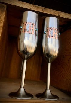 two silver wine glasses with the letters kh on them sitting next to each other