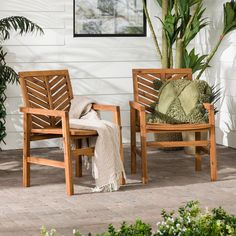 two wooden chairs sitting next to each other in front of a white wall and potted plant