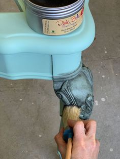 a person is holding a brush to paint a blue pot on top of a table