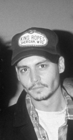 black and white photo of man wearing hat with king ropes sign on it's peak