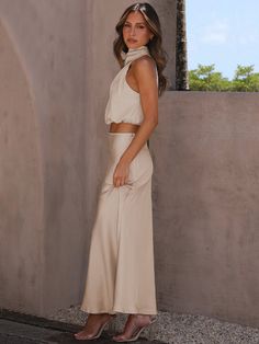 a woman standing in front of a wall wearing a white top and skirt with high slits