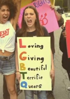 two young women holding signs and shouting in the middle of a street with other protestors