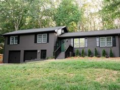 a black house with two garages and trees in the background