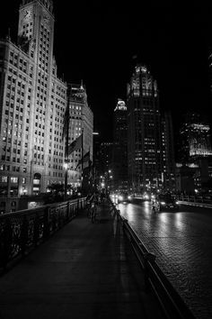 a black and white photo of the city at night with lights reflecting off water in front of tall buildings