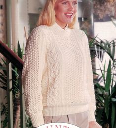 a woman in a white sweater and tan pants is smiling for the camera while standing next to a potted plant