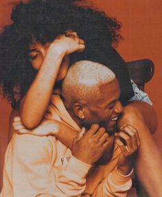 a man and woman hugging each other with an afro hairstyle on their head, in front of a brown background