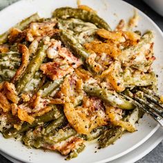 a white plate topped with green beans covered in toppings and a fork next to it