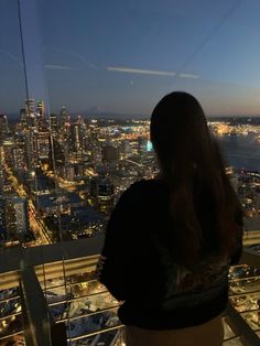 a woman standing on top of a tall building looking out at the city lights and water