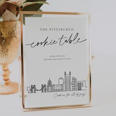 the pittsburgh cookie table sign is next to a gold vase with greenery in it