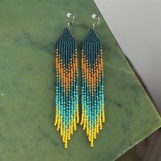 Amazing handmade seed bead earrings with beautiful green-yellow-turquoise-orange design. Emphasize your beauty and personality - be beautiful and brilliant every day! 🔎Size of Earrings with hooks: 15 cm (5.9") long and 2.5 cm (0.98") wide. Beadwork part: 13.2 cm long. I use only high-quality material in creating my works - that's why this thing will please you for a long time and will not cause any trouble in using! This Earrings comes packed in a beautiful box, ready to give as a gift! Earrings are sewed with nylon thread. I wax thread to keep earrings shape as firm and steady as possible. They may occasionally roll up while wearing, as every other beaded items. So you have to flatten them by hands. Lifehack. If you want for earrings to be firm, you can use a hairspray. Flatten an earrin Yellow Dangling Beads Earrings For Summer, Summer Yellow Dangling Beads Earrings, Yellow Summer Earrings With Dangling Beads, Summer Yellow Earrings With Dangling Beads, Yellow Beaded Earrings With Fringe, Yellow Fringe Beaded Earrings With Round Beads, Green Beaded Earrings With Fringe For Summer, Bohemian Yellow Beaded Dangle Earrings, Bohemian Yellow Beaded Earrings For Summer