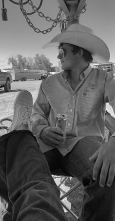 a man in a cowboy hat sitting on a bench with his feet up and holding a drink