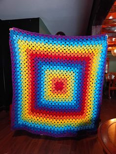 a colorful crocheted square is displayed on a wooden floor in front of a fireplace