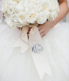 a bride holding a bouquet of white roses with the monogrammed initials on it