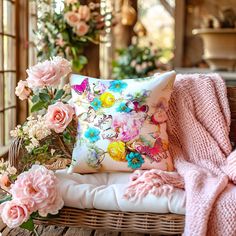 a basket filled with pink flowers next to a blanket and pillow on top of a chair