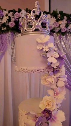 a three tiered cake with flowers and a crown on top is decorated with purple roses