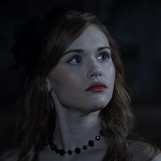 a woman with long hair wearing a black necklace and pearls on her neck is staring into the distance