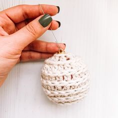 a hand holding a needle and thread over a crocheted ball ornament