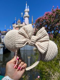 a person holding up a knitted bow in front of a castle with pink flowers