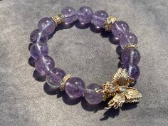 Size: 5.5-7.0inch 11mm This bracelet features natural amethyst beads, approximately 11cm, adorned with a gold-plated cubic zirconia butterfly. The design inspiration comes from the graceful elements of nature, evoking the light purple of lavender and the delicate flight of butterflies. This piece combines the mysterious allure of natural amethyst with the splendid elegance of gold-plated cubic zirconia, showcasing a blend of natural beauty, peace, and grace. Elegant Amethyst Crystal Bracelet With 8mm Beads, Spiritual Amethyst Gold Bracelets, Gold Beaded Bracelets With Gemstone Accents, Elegant Purple Crystal Bracelet For Healing, Gold Amethyst Jewelry With 8mm Beads, Luxury Gold Amethyst Bracelets, Gold Amethyst Beaded Bracelets, Gold Amethyst Beaded Bracelets For Jewelry Making, Gold Amethyst Bracelets For Healing