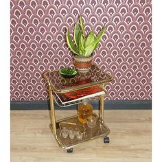 a gold serving cart with a potted plant on top and glasses on the bottom