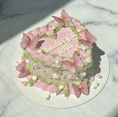 a pink and green birthday cake with butterflies on it's top sitting on a marble table