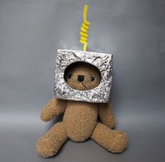 a teddy bear is wrapped in tin foil and has a yellow cord hanging from it's head